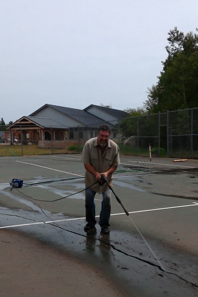 Marc Smith pressure washing the cracks on the tennis court in preparation for patching.